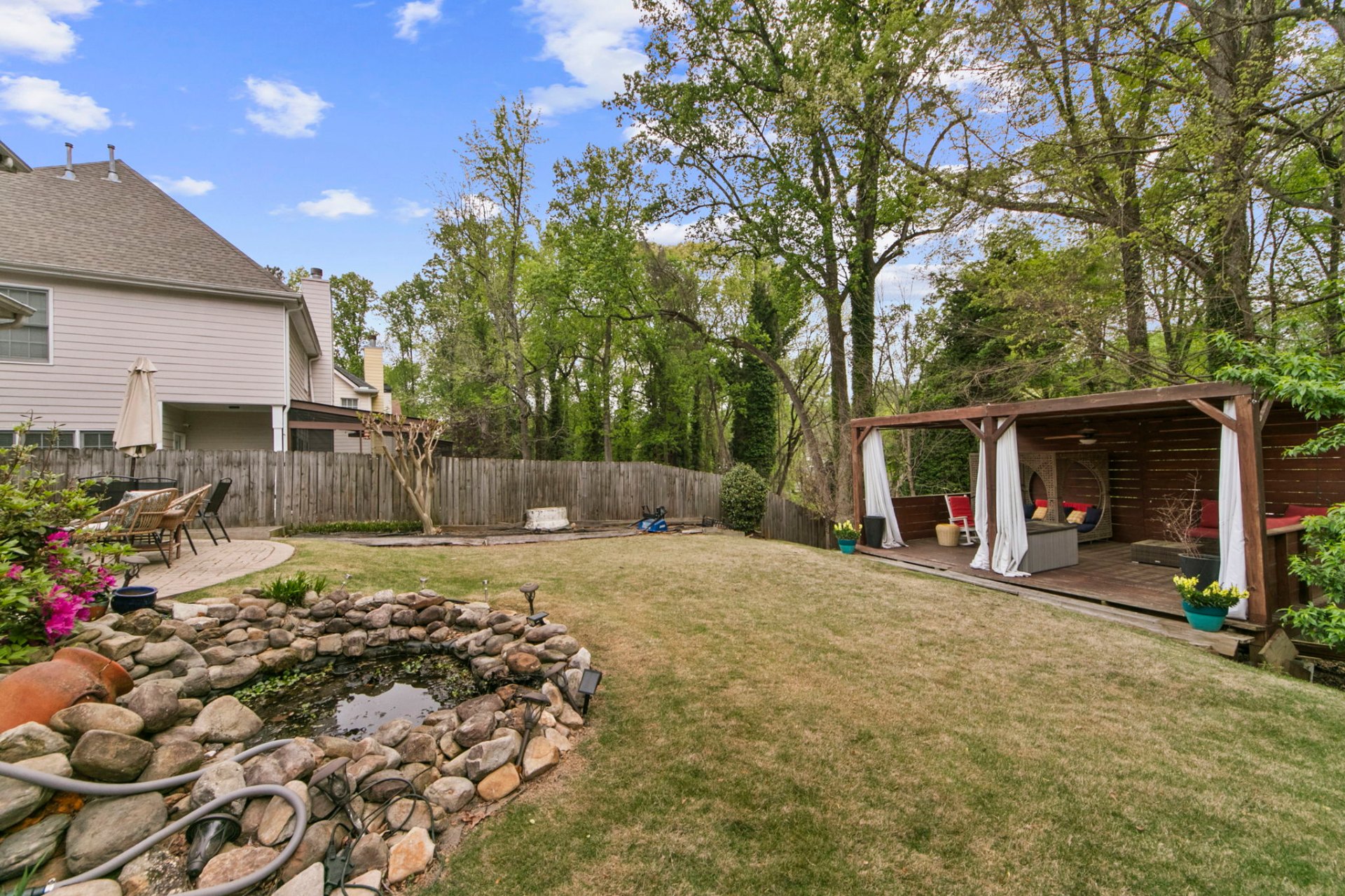 Fenced backyard at 4081 Tilly Mill Rd with koi pond, Zoysia lawn, and covered cabana with curtains